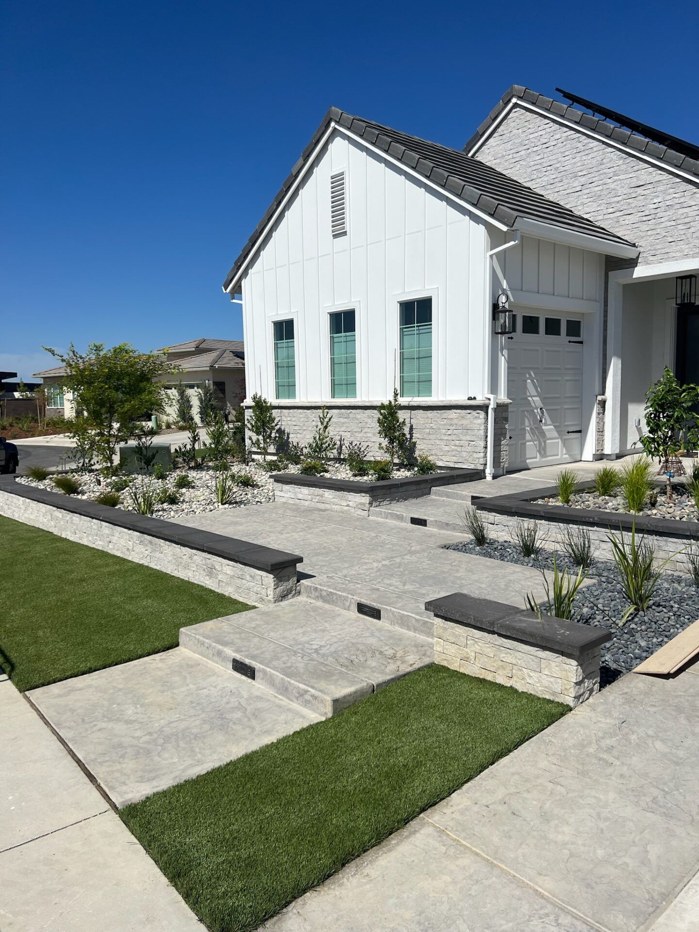 Exterior of a modern house with white siding, garage, and landscaped yard with artificial grass and stone pathways.