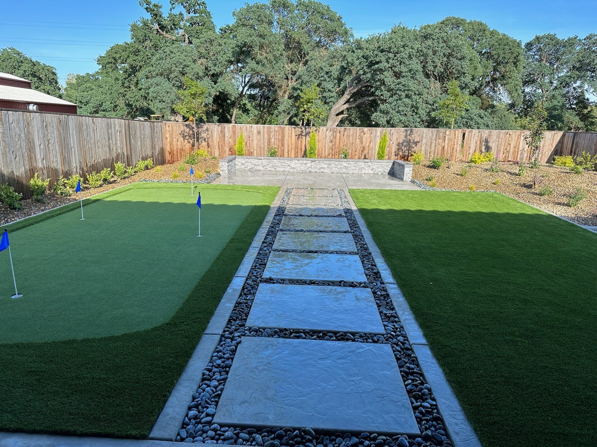 Backyard with a putting green, stone walkway, and wooden fence.