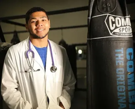 A man in a lab coat with a stethoscope around his neck is standing next to a boxing bag.