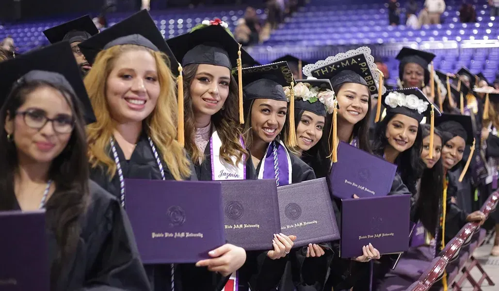 A group of women in graduation caps and gowns are holding their diplomas.