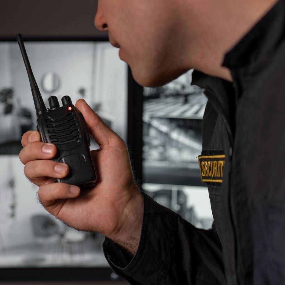 Guardia de seguridad hablando por un walkie-talkie, mirando cámaras de seguridad, vistiendo uniforme.