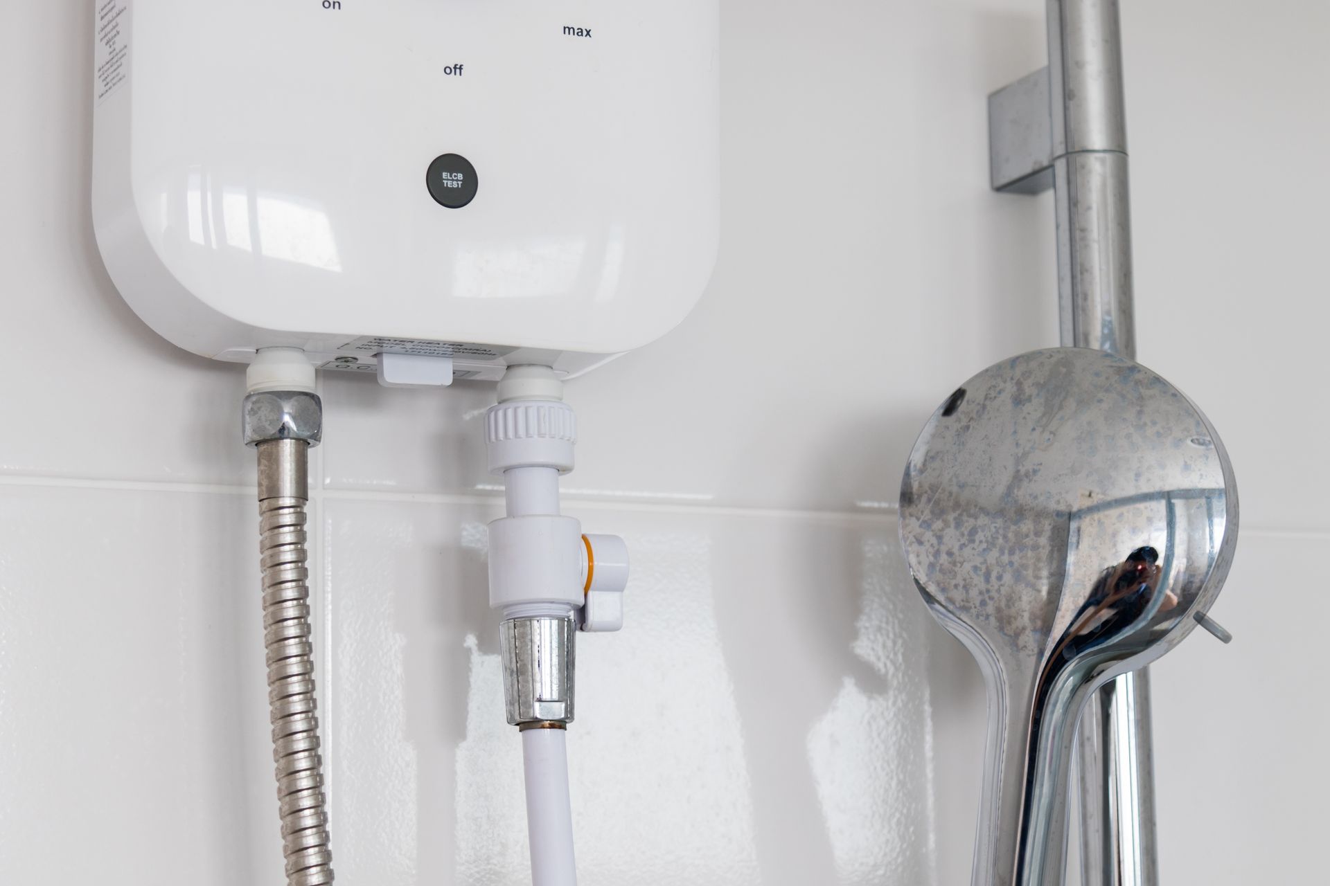 Tankless electric water heater installed on white tile wall.