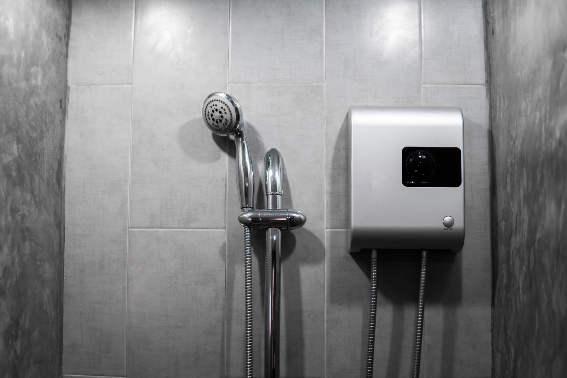 Tankless water heater installed on grey tile wall.