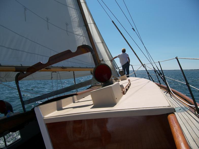 A man stands on the deck of a sailboat in the ocean