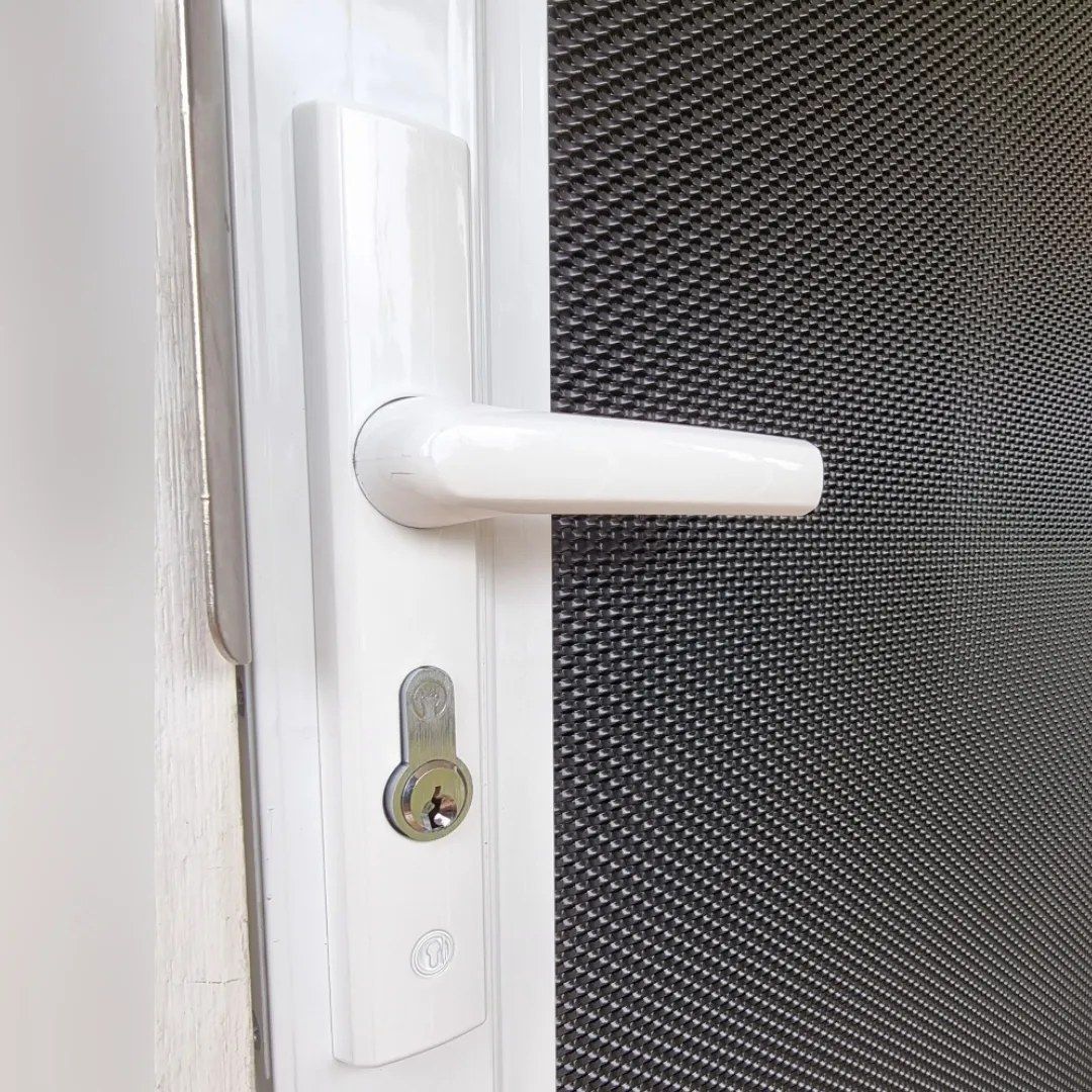 A close up of a white door handle on a screen door.