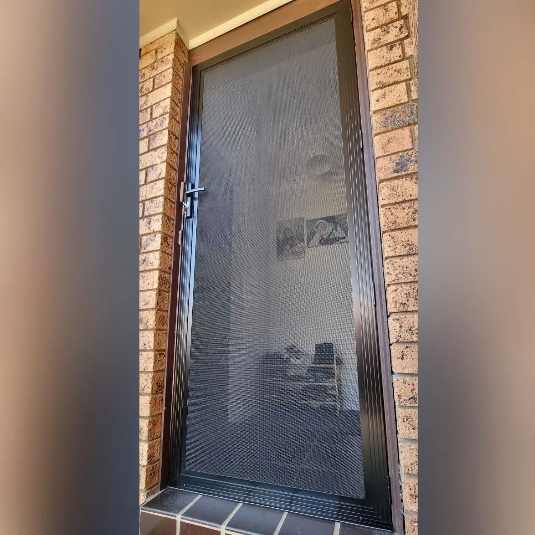 A black screen door is on a brick wall.