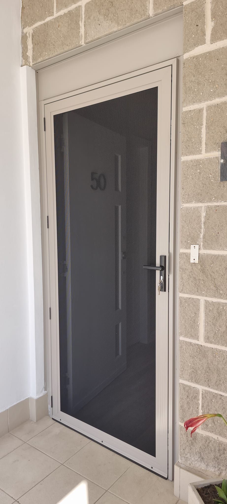 A screen door is sitting on a tiled floor next to a brick wall.