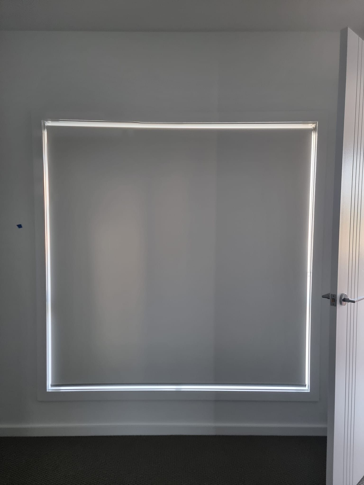 A square window with a blind on it in a room with a door open.