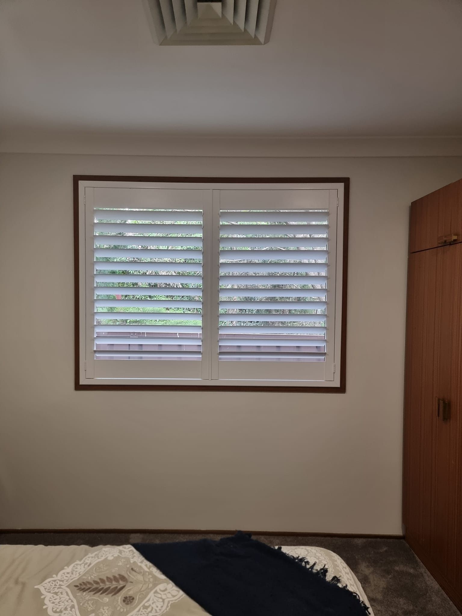 A bedroom with a bed and a window with shutters on it.