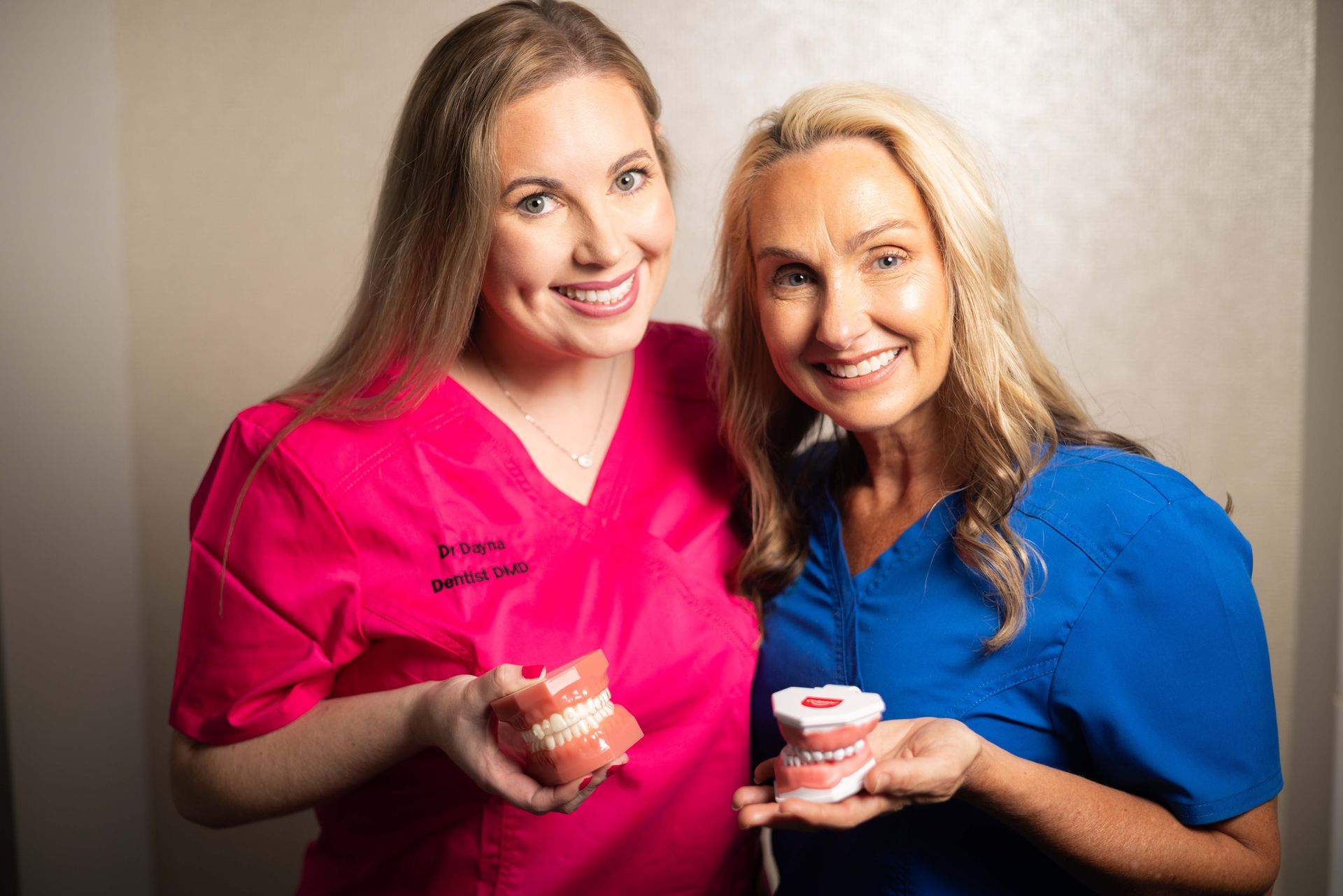 Two women are standing next to each other holding dental models.