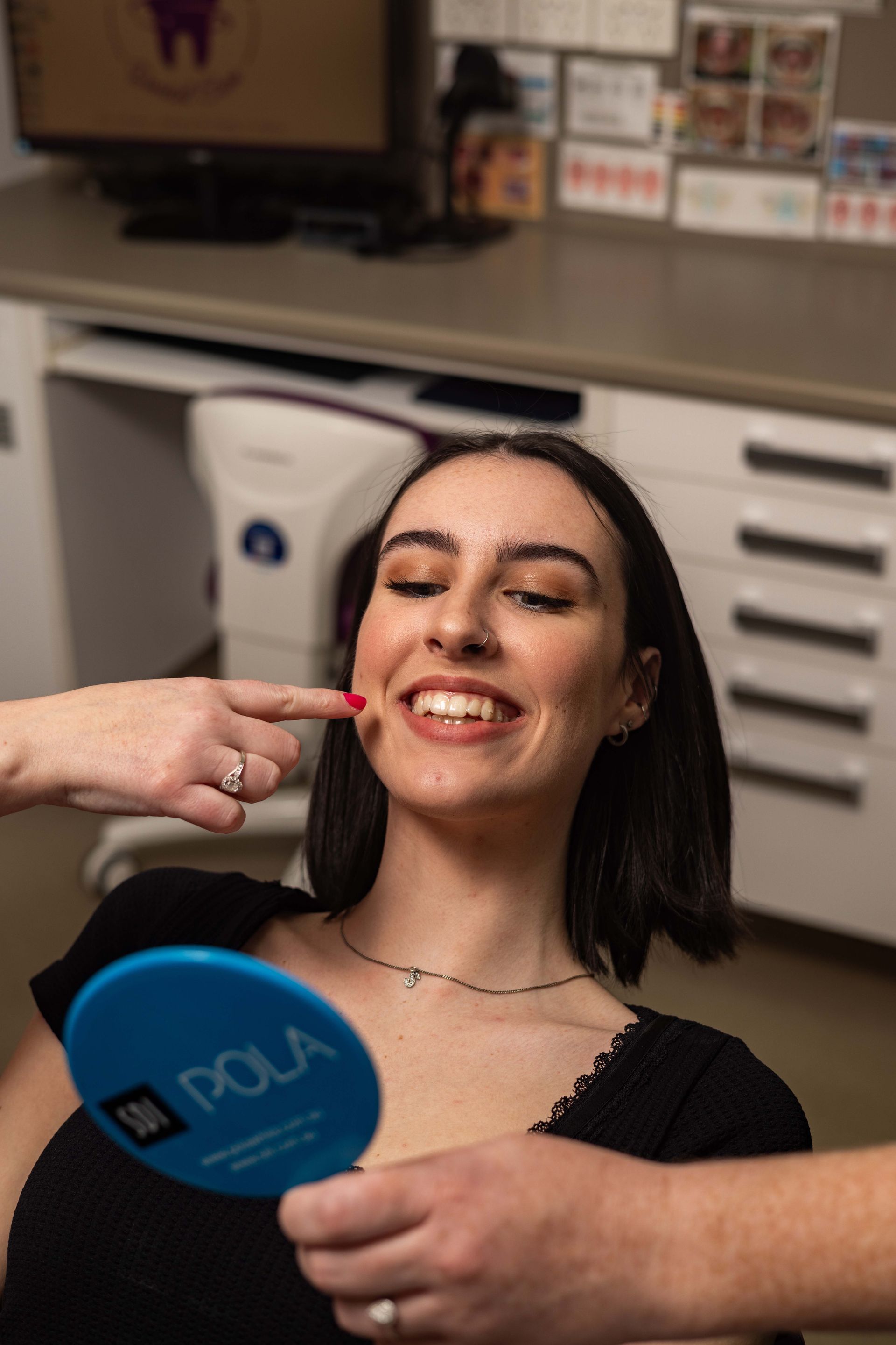 A woman is smiling while looking at her teeth in a mirror.