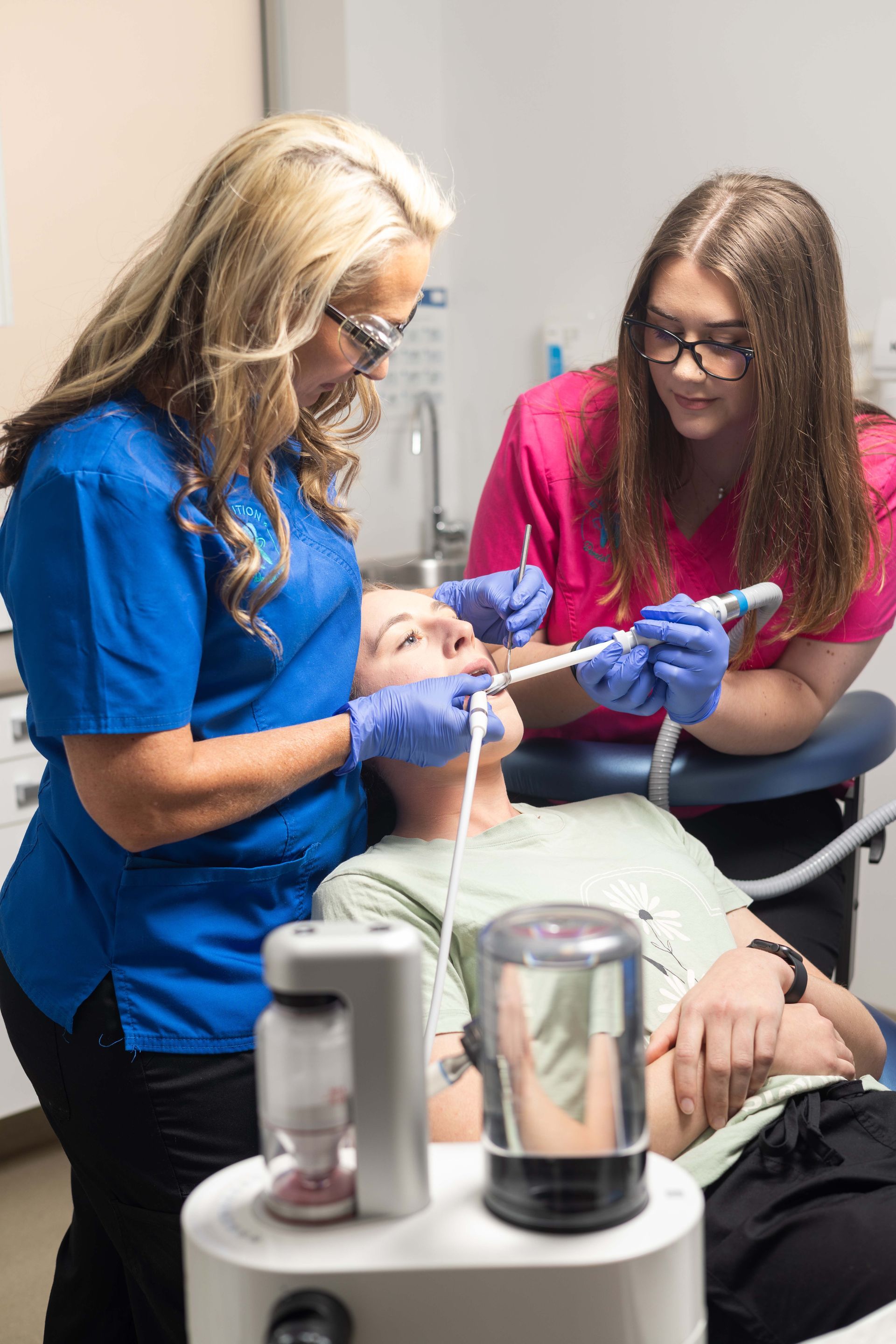 Two female dentists are examining a patient's teeth in a dental office.