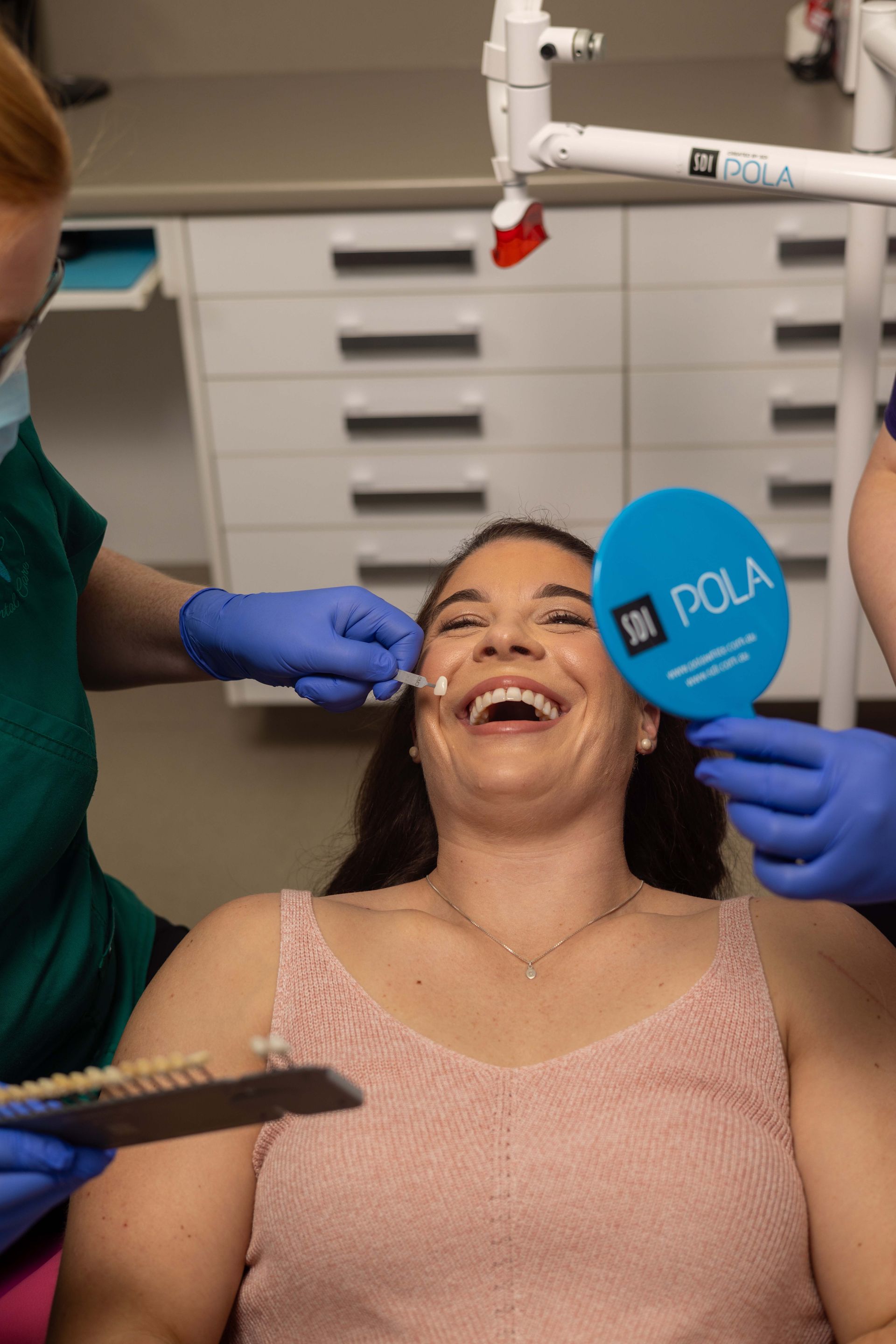 A woman is sitting in a dental chair while a dentist examines her teeth.