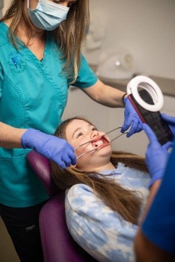 A dentist is examining a young girl 's teeth in a dental chair.