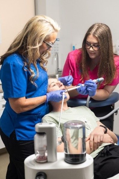 Two female dentists are examining a patient 's teeth in a dental office.