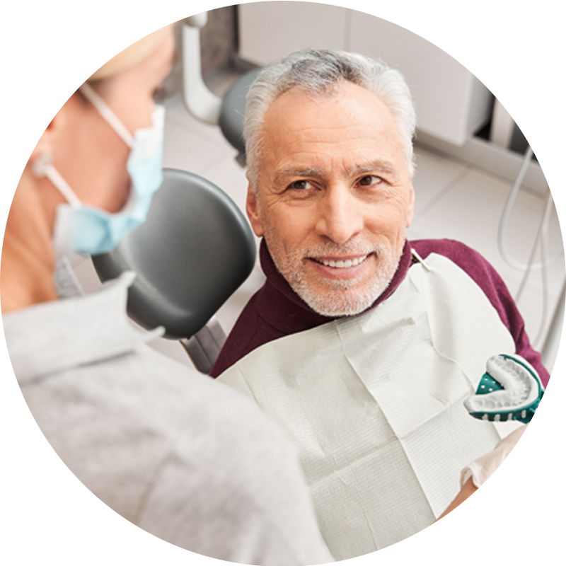 An older man is sitting in a dental chair talking to a dentist.