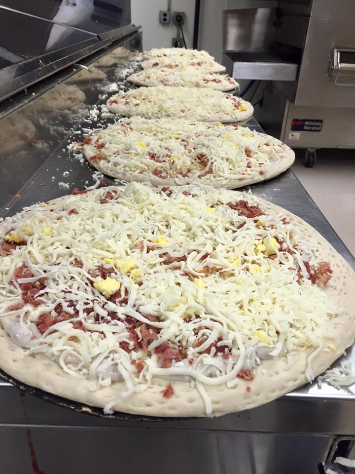 A row of pizzas sitting on top of a stainless steel counter.