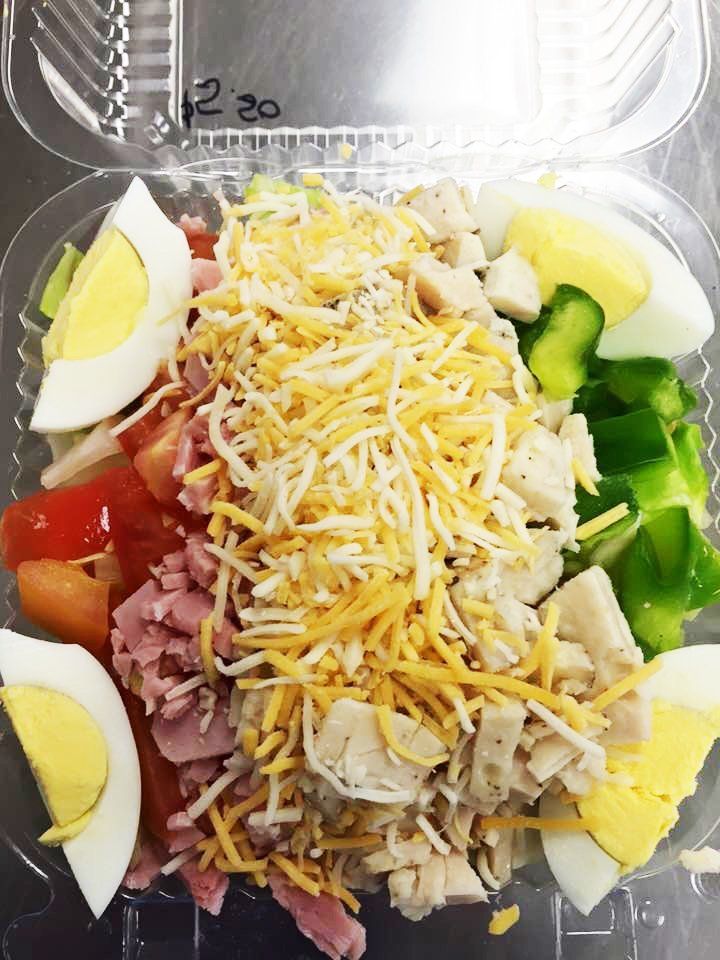 A salad with ham , cheese , eggs , tomatoes and cucumbers in a plastic container.