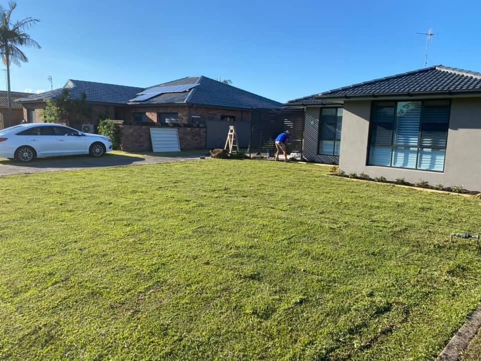 A Person Mowing a Lawn in Front of Houses With Solar Panels on the Roofs Under a Blue Sky — Coastal Slashing & Mowing Services In Forster, NSW