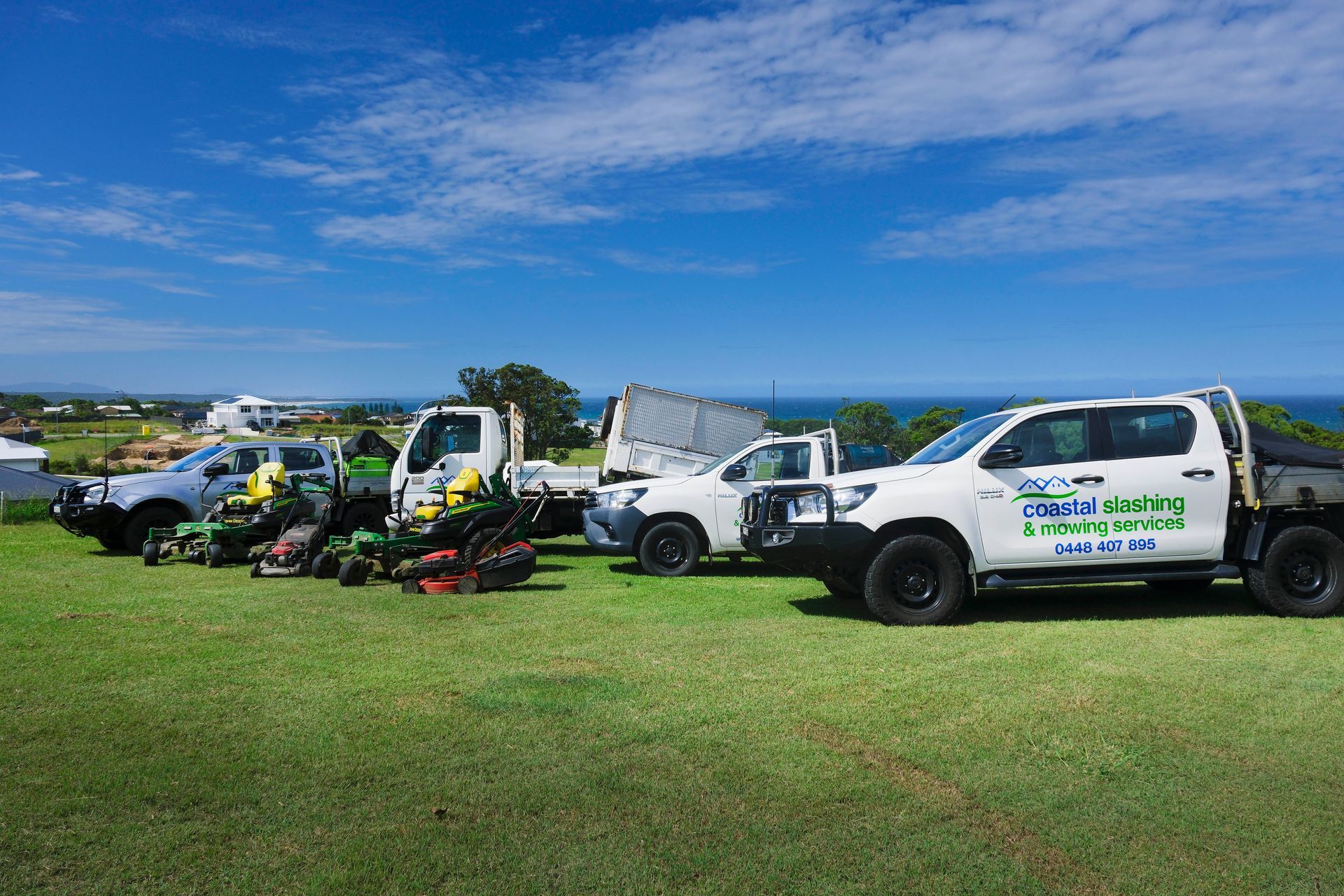 A Line of White Work Trucks and Green Lawn Mowers Parked — Coastal Slashing & Mowing Services In Hallidays Point, NSW