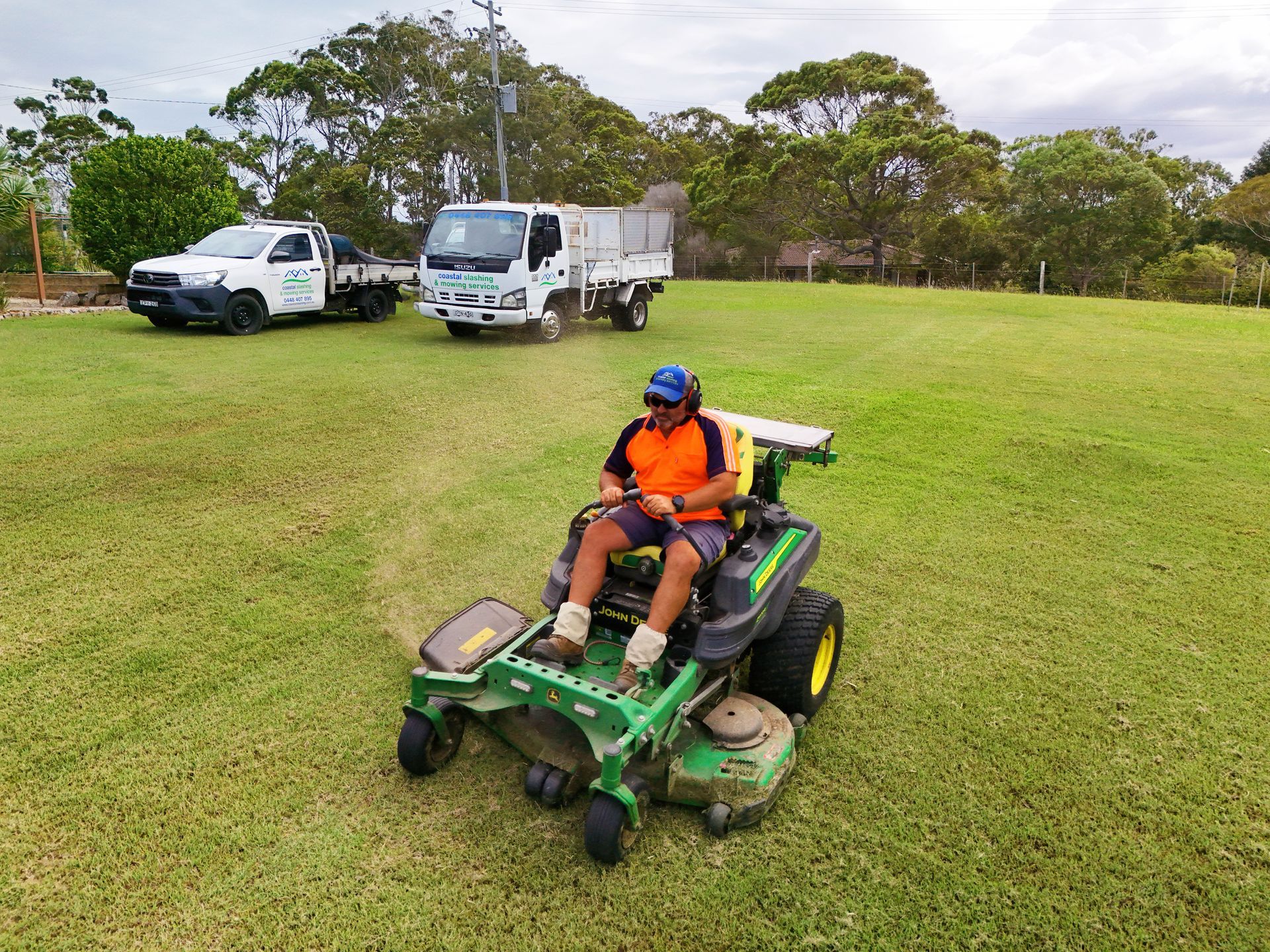 A Person in High-visibility Work Clothes Drives a Green Zero-turn Mower — Coastal Slashing & Mowing Services In Wingham, NSW