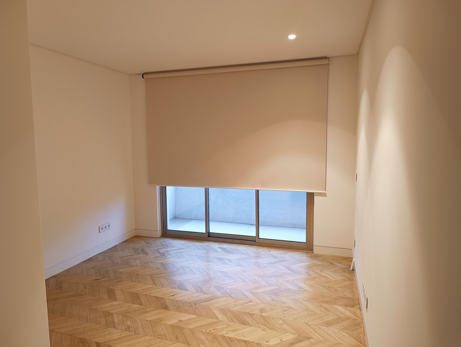 Quarto vazio com persiana bege cobrindo uma janela, piso de parquet.