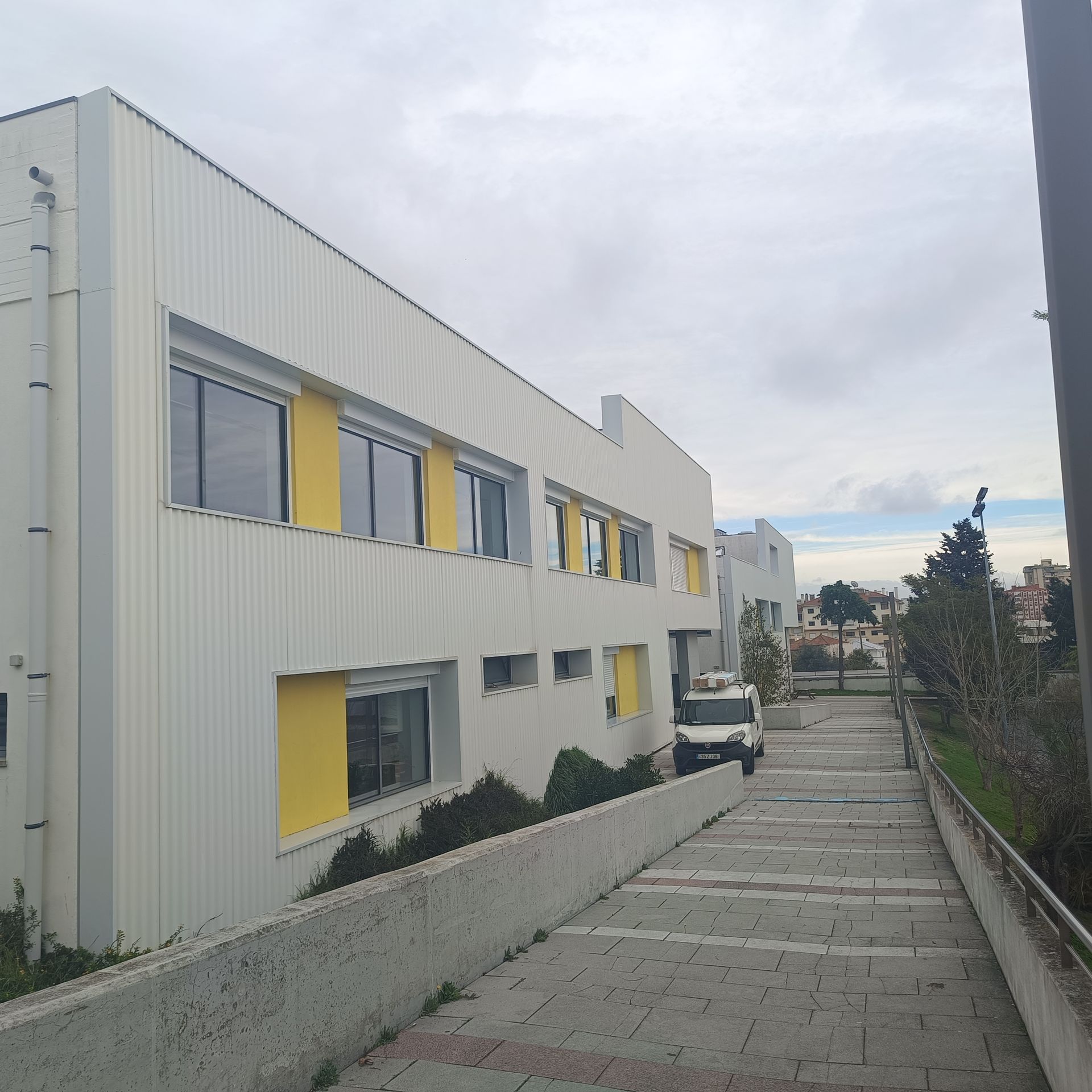 Prédio branco com molduras de janelas amarelas; caminho com degraus; céu nublado.