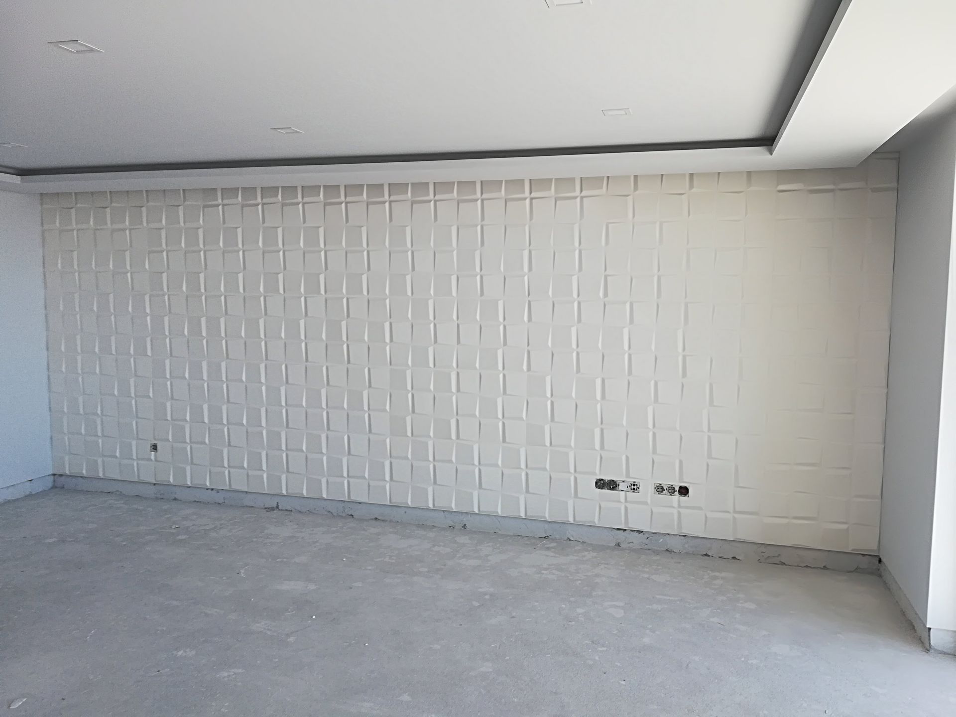 Sala vazia com parede texturizada branca como destaque, piso de concreto e iluminação embutida no teto.