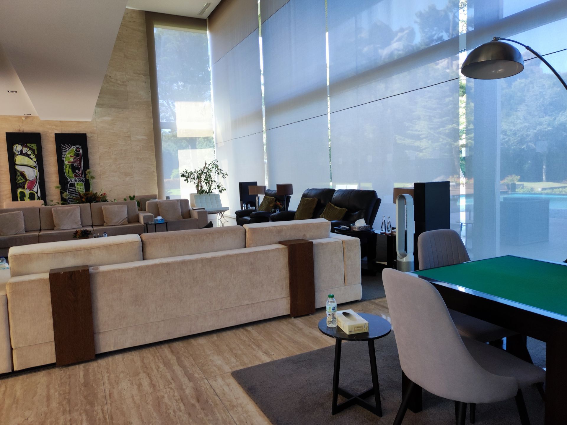 Área de estar com janelas amplas e assentos confortáveis. Inclui sofás, cadeiras e uma pequena mesa.