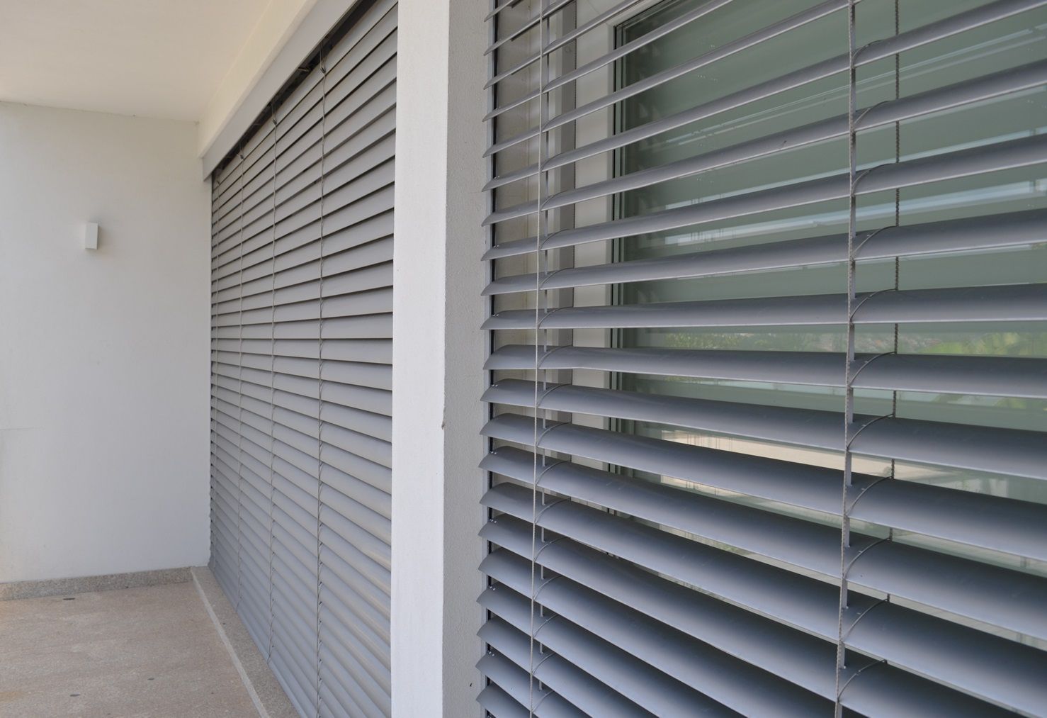 Persianas cinza com ripas cobrem uma janela e a parede da varanda.