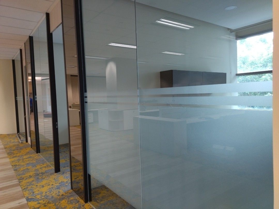 Escritório com paredes de vidro, parcialmente foscas, e carpete estampado.