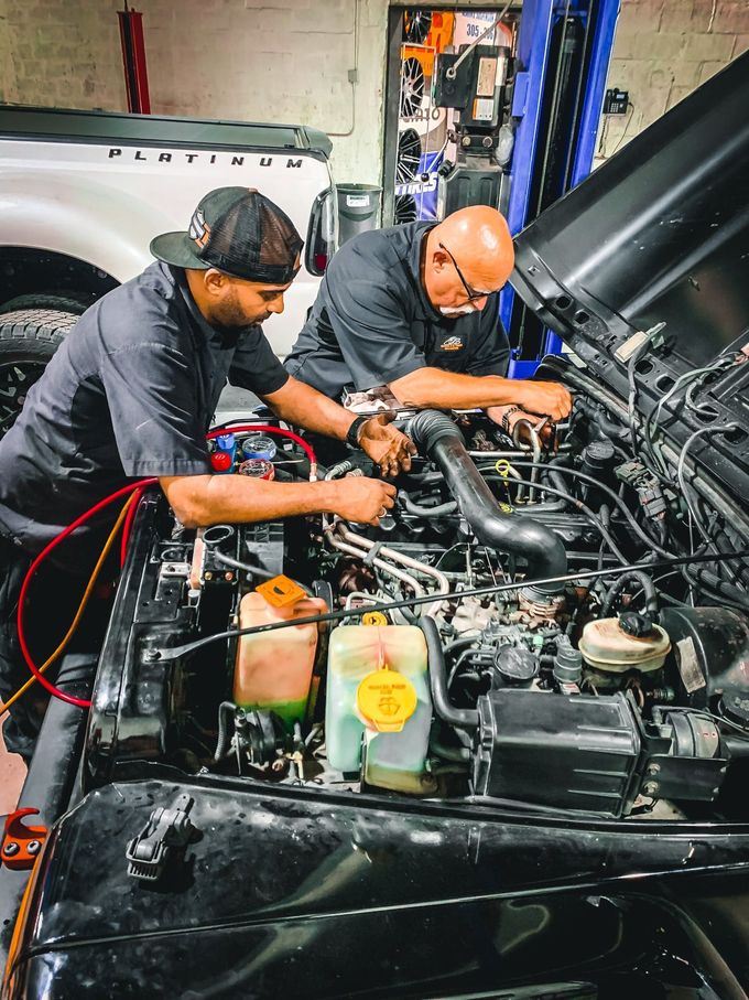 Two men are working on the engine of a car in a garage. | CB Wheels & Tires, 4x4, Suspension, Center