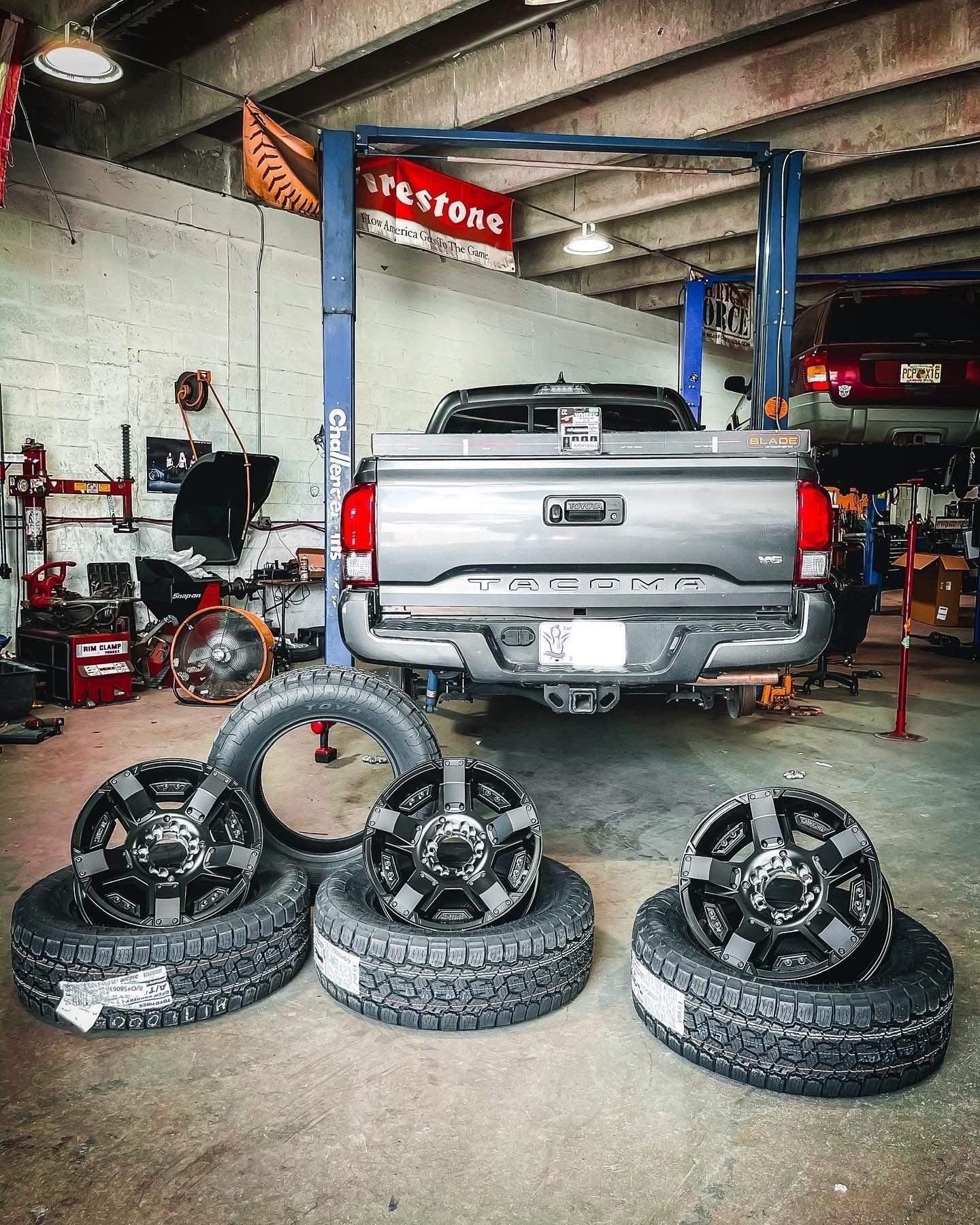 A truck is sitting on a lift in a garage next to tires and wheels. | CB Wheels & Tires, 4x4, Suspension, Center