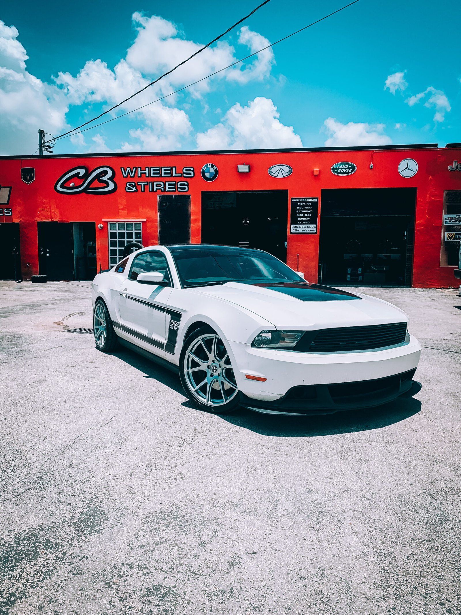 A white mustang is parked in front of a red building. | CB Wheels & Tires, 4x4, Suspension, Center