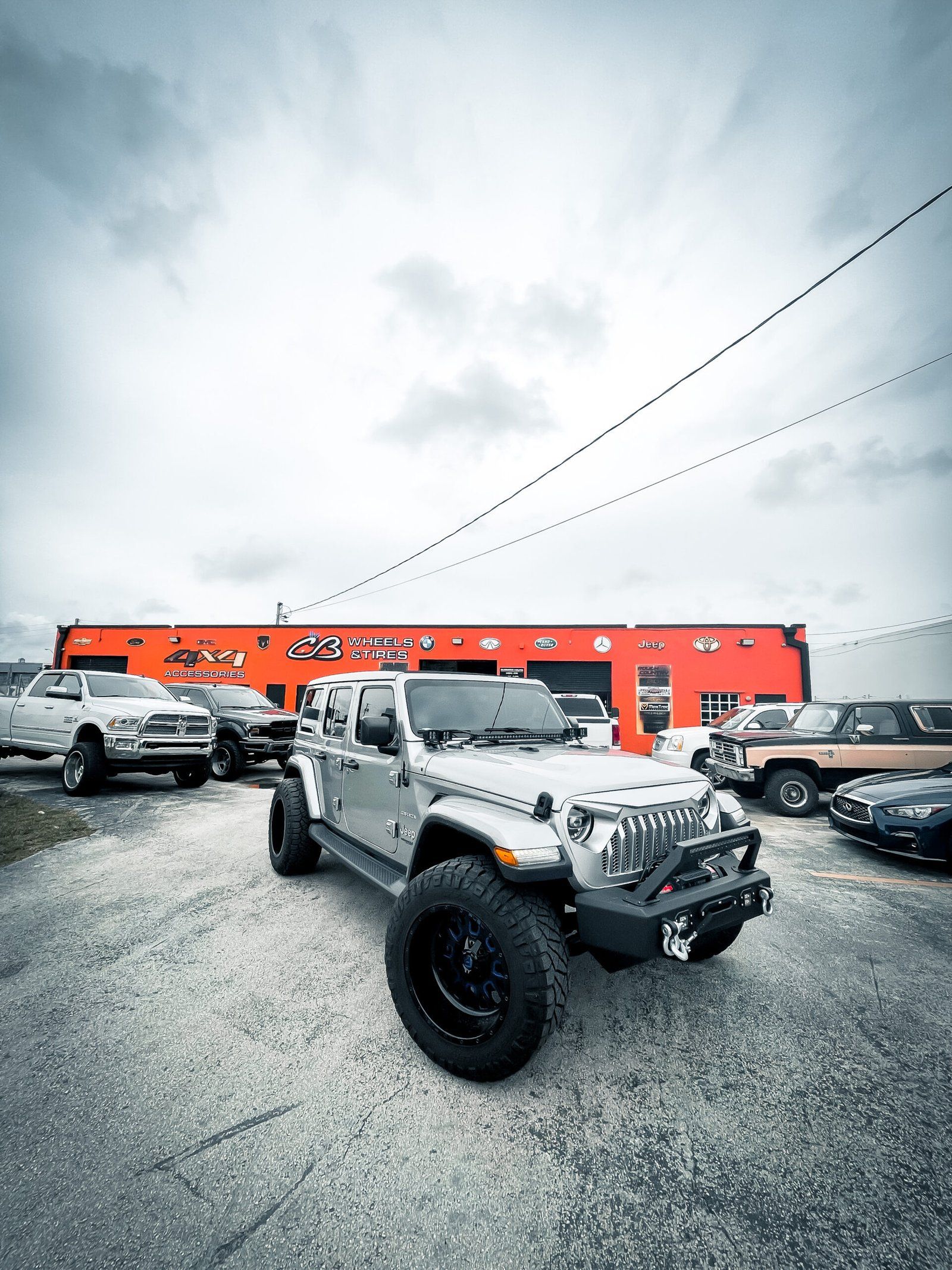 A jeep is parked in front of a car dealership. | CB Wheels & Tires, 4x4, Suspension, Center