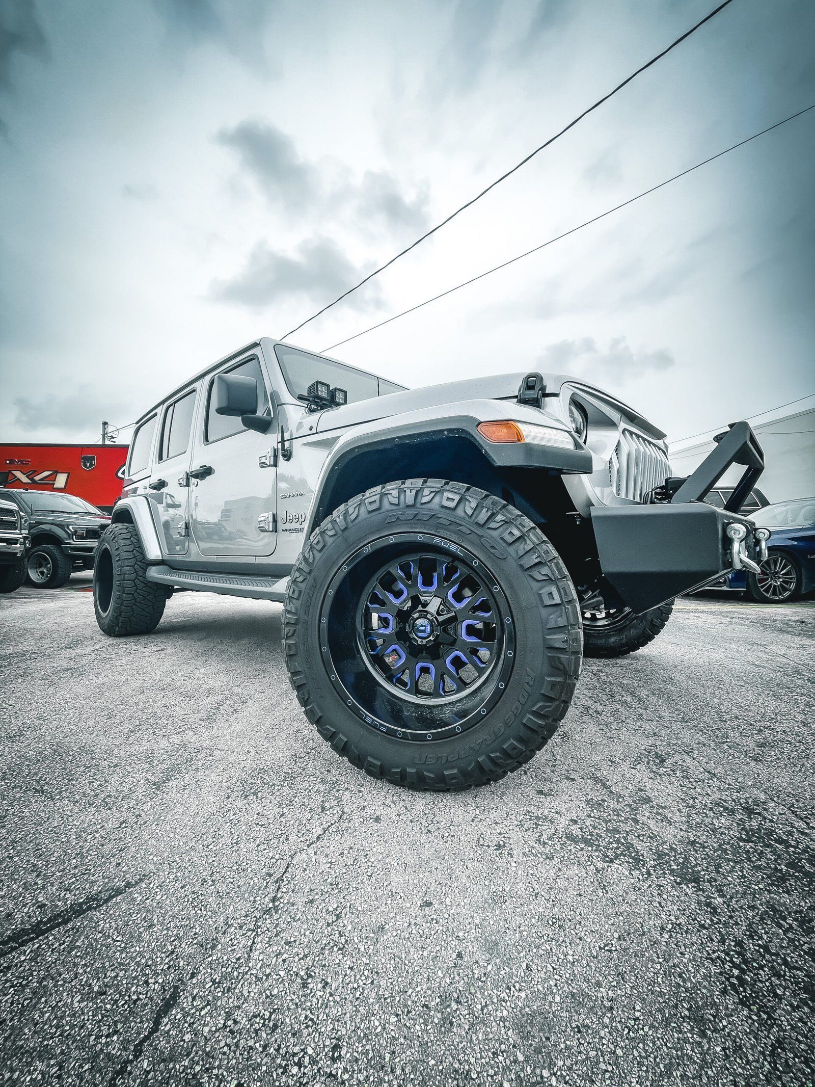 A jeep is parked in a gravel lot in front of a building. | CB Wheels & Tires, 4x4, Suspension, Center