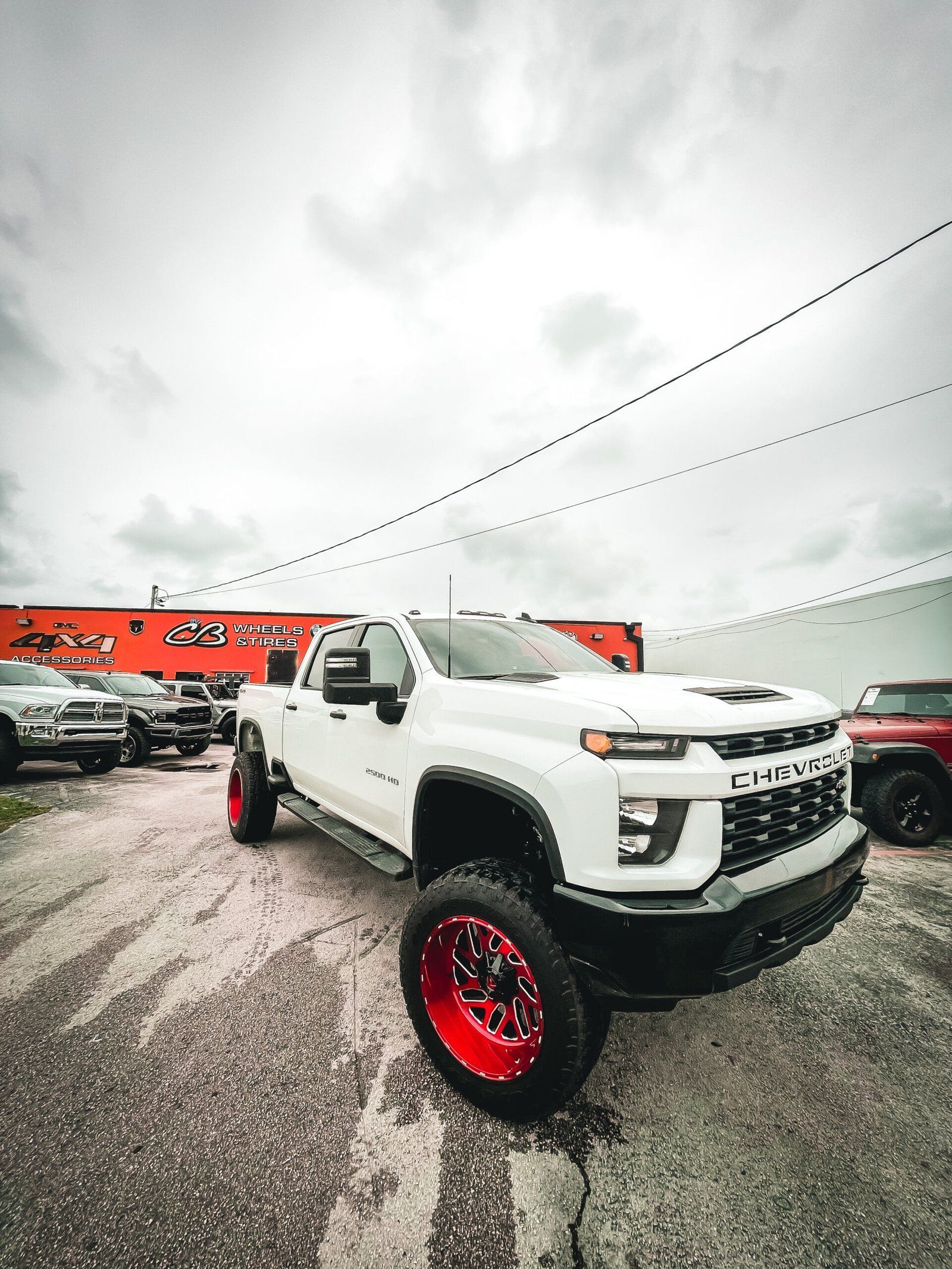 A white truck with red wheels is parked in a parking lot. | CB Wheels & Tires, 4x4, Suspension, Center
