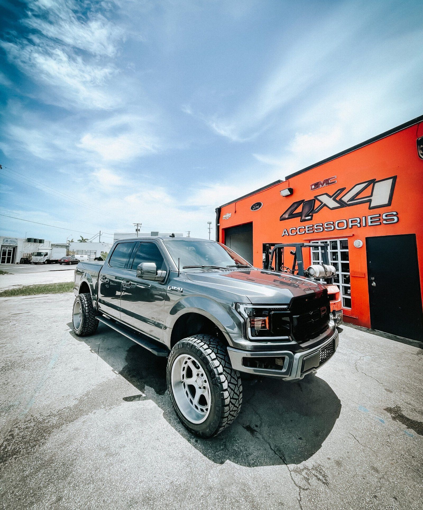 A black truck is parked in front of an orange building. | CB Wheels & Tires, 4x4, Suspension, Center