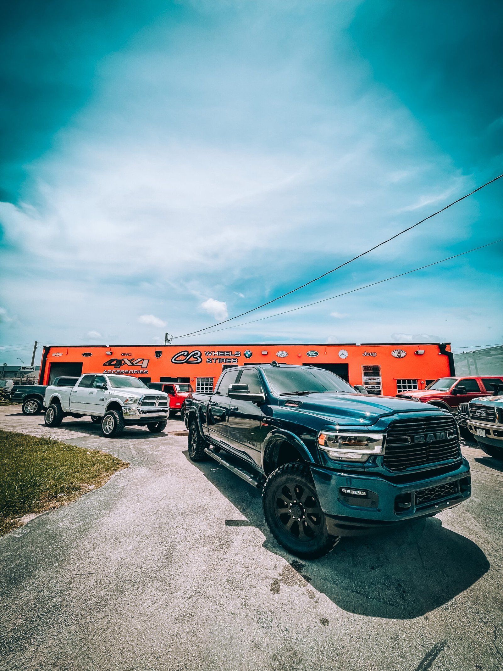 A blue ram truck is parked in front of a car dealership. | CB Wheels & Tires, 4x4, Suspension, Center