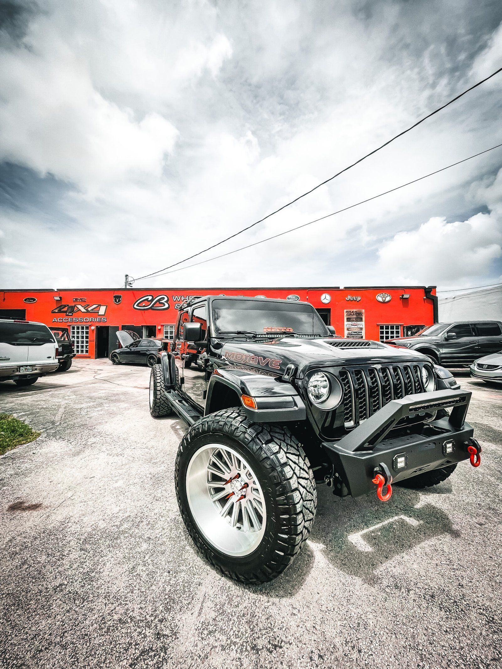 A jeep is parked in front of a car dealership. | CB Wheels & Tires, 4x4, Suspension, Center