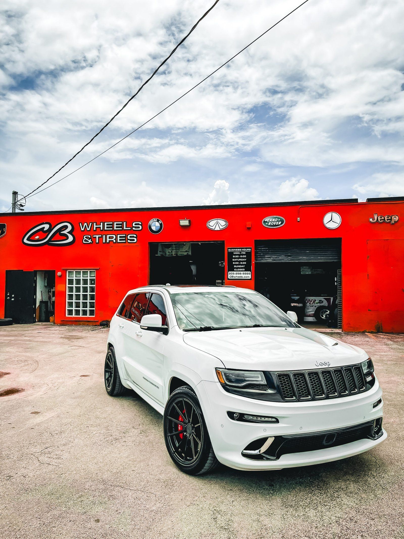 A white jeep grand cherokee is parked in front of a red building. | CB Wheels & Tires, 4x4, Suspension, Center
