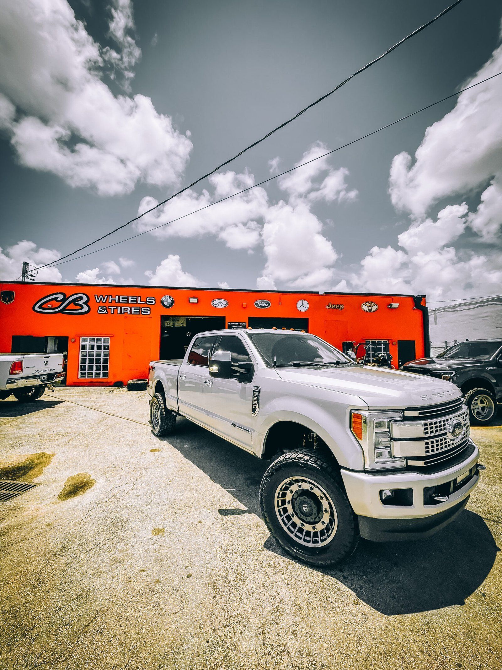 A silver truck is parked in front of an orange building. | CB Wheels & Tires, 4x4, Suspension, Center