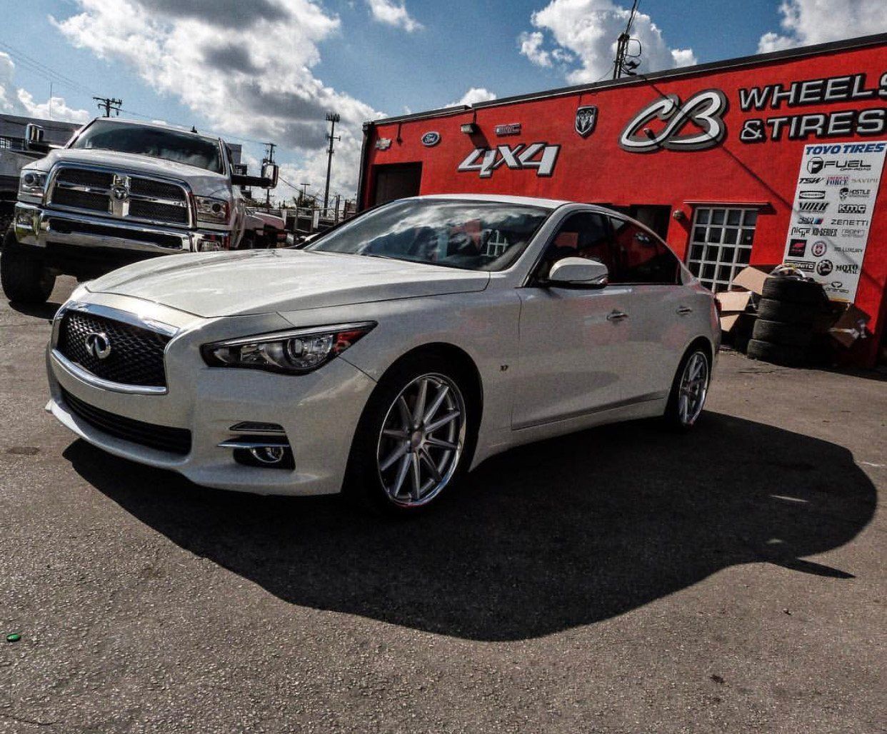 A white car is parked in front of a red building that says cb wheel & tire | CB Wheels & Tires, 4x4, Suspension, Center