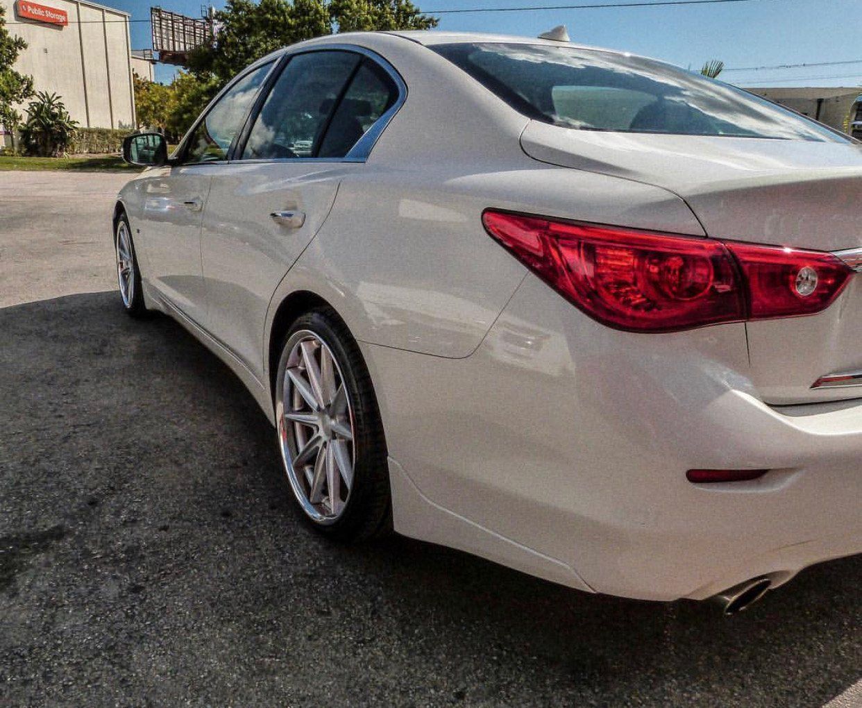 A white car with a red tail light is parked in a parking lot | CB Wheels & Tires, 4x4, Suspension, Center