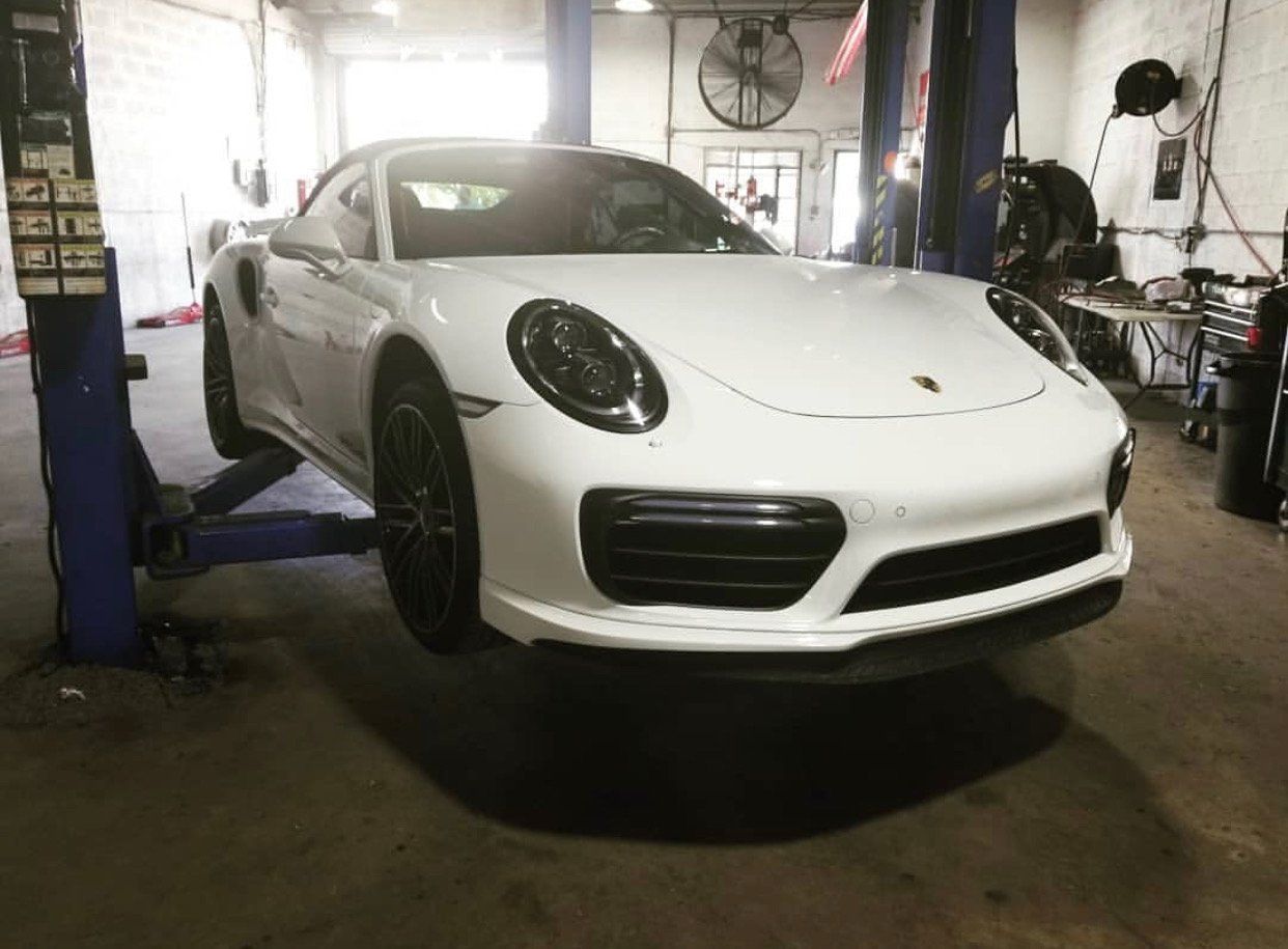 A white porsche 911 turbo s is parked on a lift in a garage. | CB Wheels & Tires, 4x4, Suspension, Center