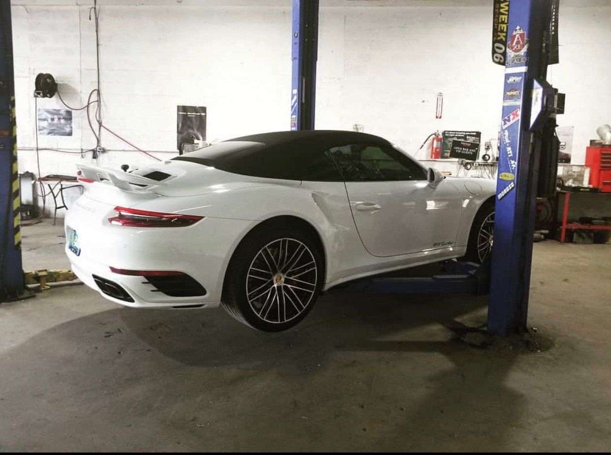 A white sports car is sitting on a lift in a garage. | CB Wheels & Tires, 4x4, Suspension, Center
