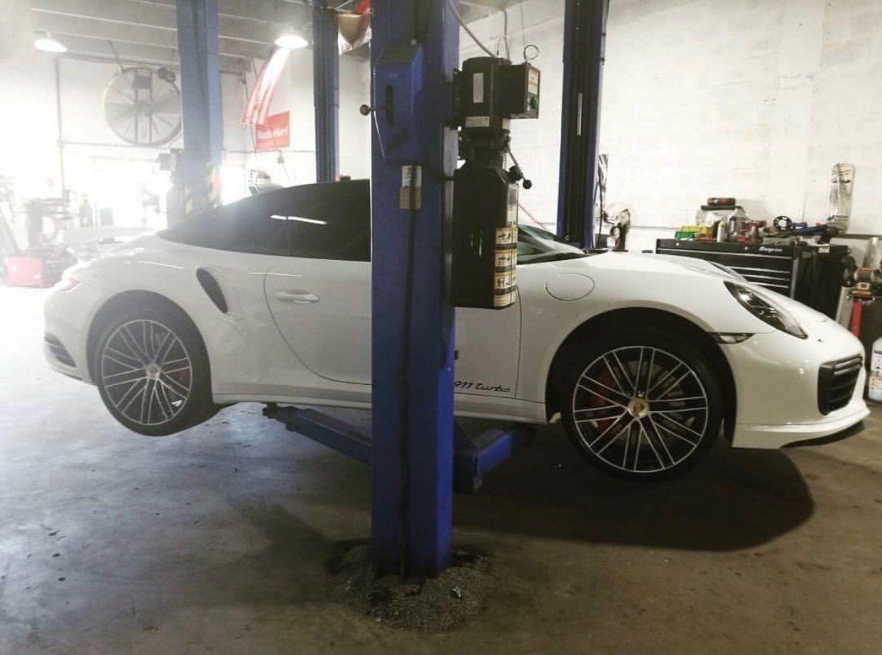 A white porsche 911 turbo is sitting on a lift in a garage. | CB Wheels & Tires, 4x4, Suspension, Center