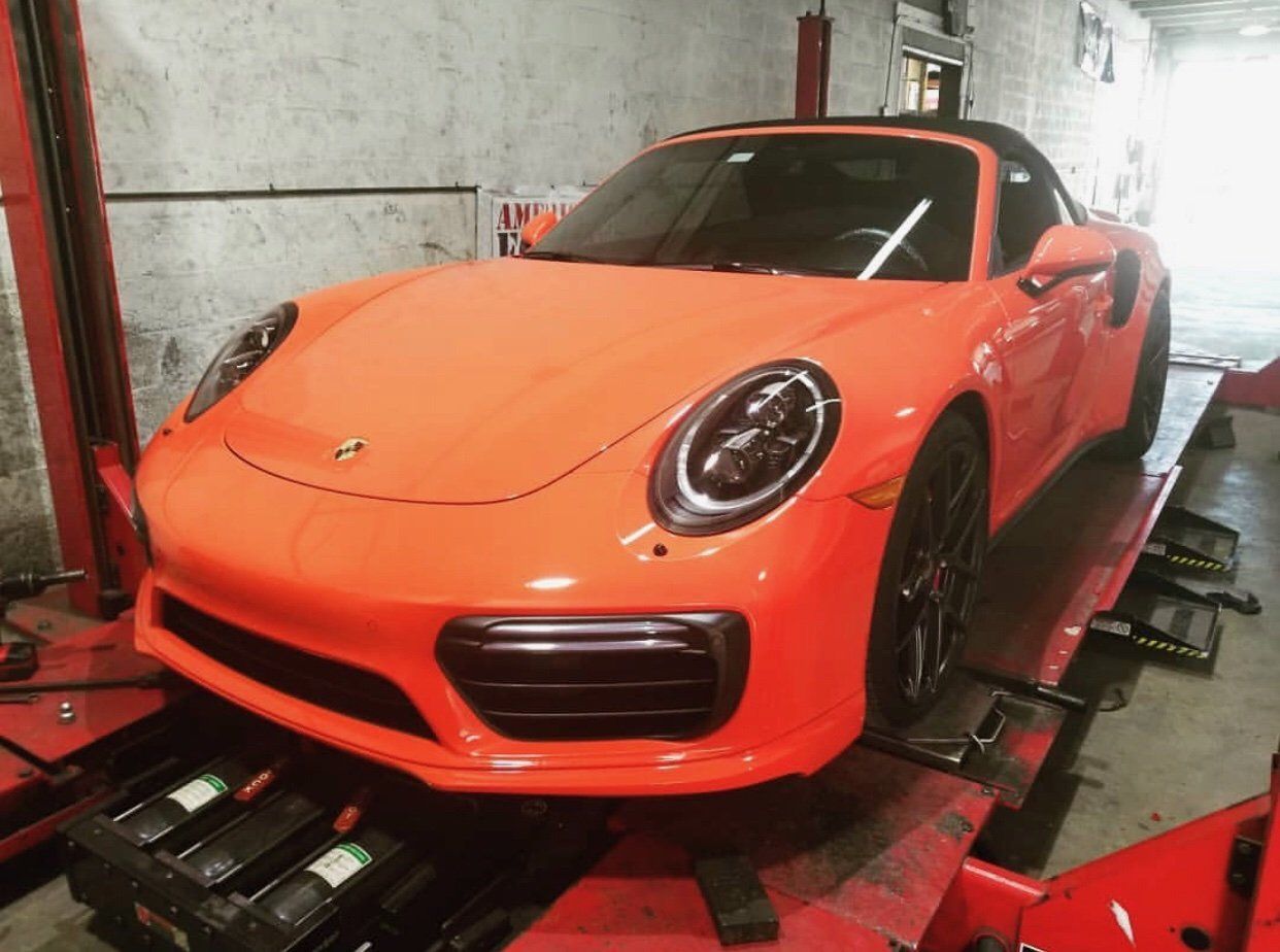 An orange porsche 911 targa turbo is sitting on a lift in a garage. | CB Wheels & Tires, 4x4, Suspension, Center