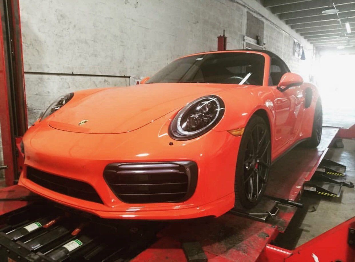 An orange porsche 911 turbo s is sitting on a lift in a garage. | CB Wheels & Tires, 4x4, Suspension, Center