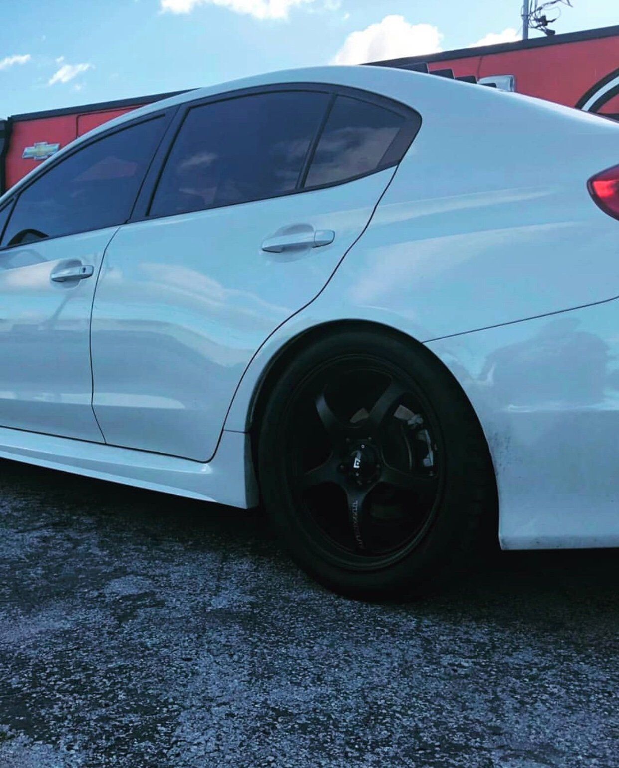 A white car with black wheels is parked in a gravel lot. | CB Wheels & Tires, 4x4, Suspension, Center
